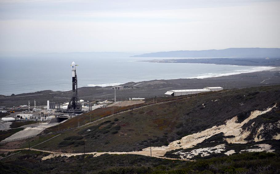 A rocket is on a launch pad beside an ocean coastline.