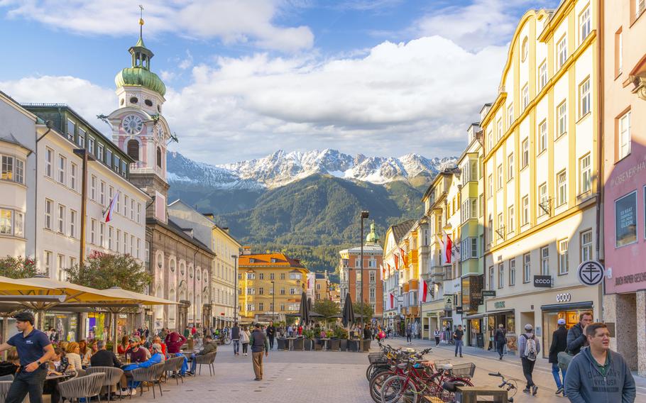 A pedestrian street is flanked by city buildings in the Alpine style, with a few of the mountains in the distance, in Innsbruck, Austria.