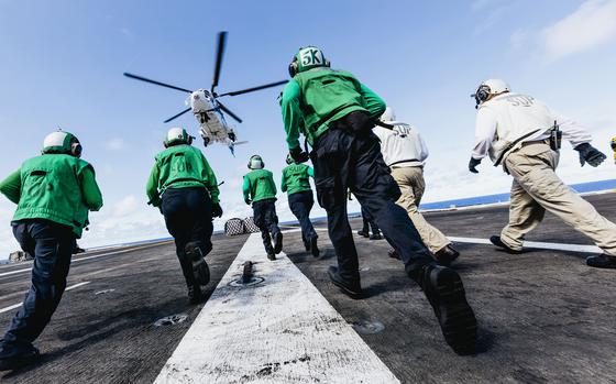 Sailors run toward cargo on the flight deck of the USS George Washington that was dropped off by helicopter while underway in the Pacific Ocean, Oct. 24, 2024.