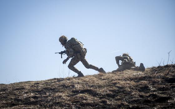 A cadet runs while holding a gun and another takes cover during a live-fire platoon attack at Grafenwoehr Training Area in Germany .