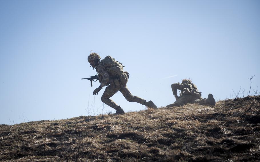 A cadet runs while holding a gun and another takes cover during a live-fire platoon attack at Grafenwoehr Training Area in Germany.