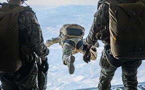 A military service member wearing a parachute jumps out of a plane over Serbia as two others look on.