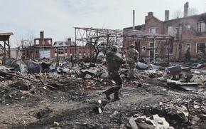 Two Russian soldiers in the combat gear walk past the rubble of destroyed buildings while other soldiers are seen in the background.