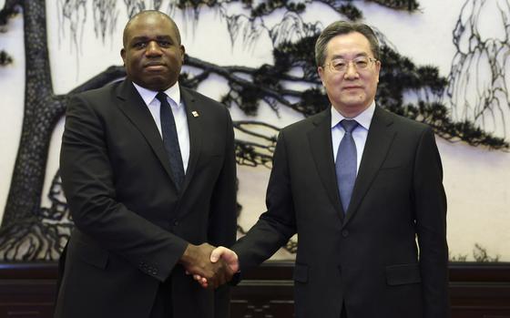 British Foreign Secretary David Lammy and Chinese Vice Premier Ding Xuexiang shake hands in front of a large tapestry.