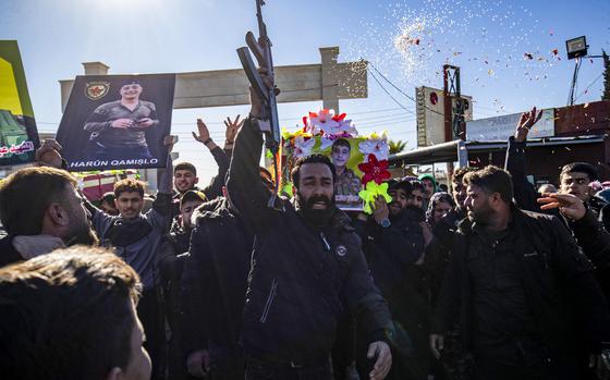 A public funeral for fighters of the Syrian Democratic Forces, with a man in the center raising a rifle to the sky with one hand.