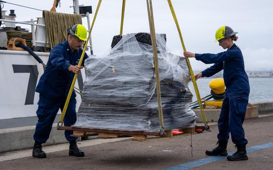 Two Coast Guard crew members guide a palate with a bale of cocaine hoisted from the ship.