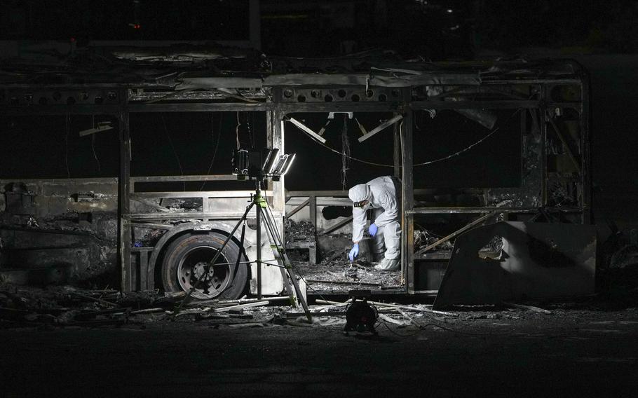 A man in a protective hazmat suit bends over to collect evidence in the charred remains of a destroyed bus.