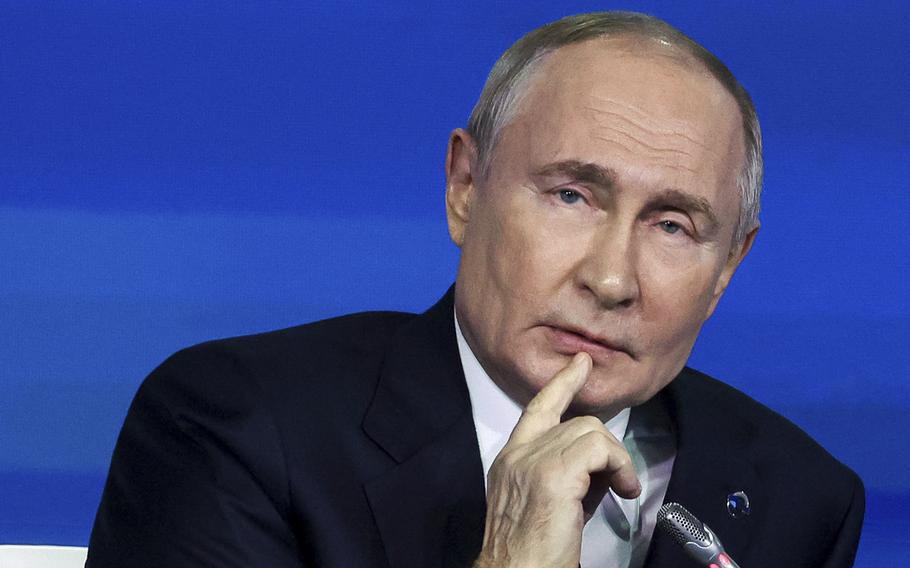 Vladimir Putin sits at a microphone during a meeting with policy experts.