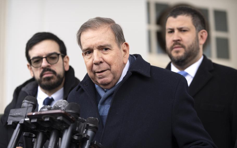 Edmundo Gonzalez in the center of the image with two men standing behind him and a series of microphones in front of him.