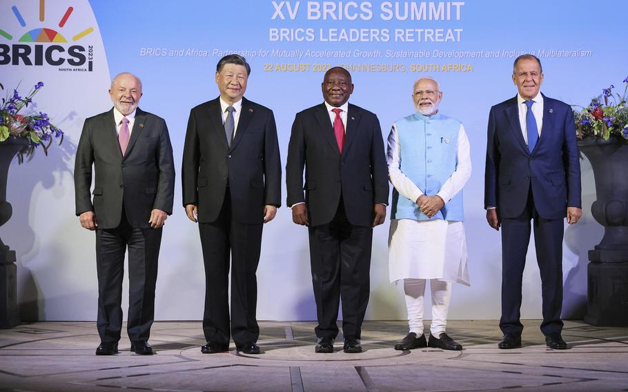 The leaders of Brazil, China, South Africa and India and the foreign minister of Russia smile for a family photo against a poster.