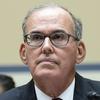 Close-up view of a man in glasses and a dark suit at a congressional hearing.