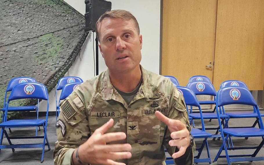 An Army colonel, seated, speaks from inside a building.