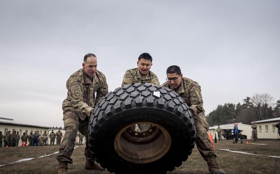 Three U.S. soldiers flip a tire during a relay contest.