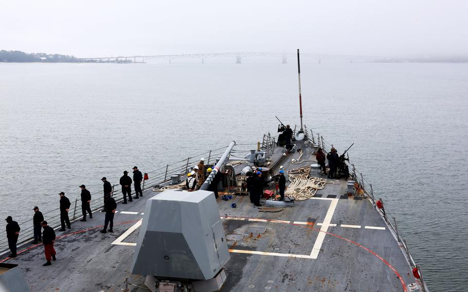 Sailors on the deck of a ship as it sails down a river.