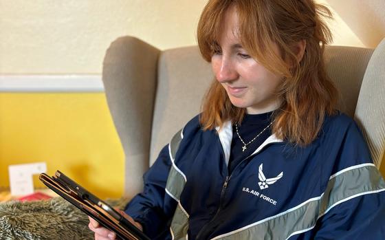 A woman in an Air Force jacket watches streamed content on a tablet.