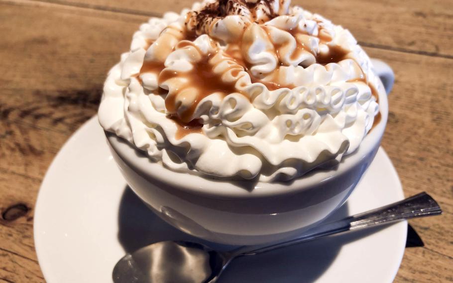 A white coffee cup is piled high with a mountain of whipped cream and caramel sauce.