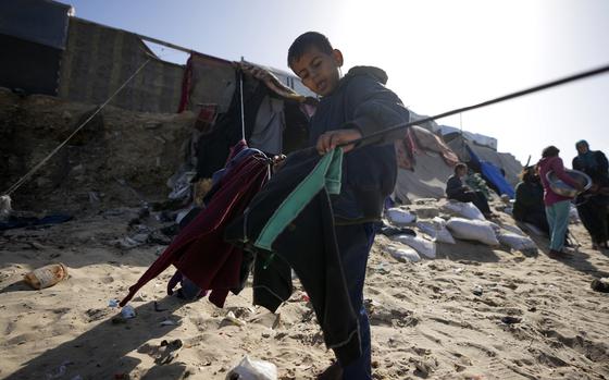 A Palestinian child hanging cloths on a rope outside tents made locally from pieces of cloth and nylon, in a camp for internally displaced Palestinians at the beachfront in Deir al-Balah, central Gaza Strip, Friday, Dec. 27, 2024. (AP Photo/Abdel Kareem Hana)