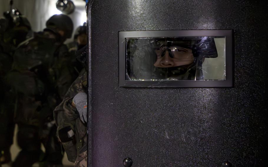 A South Korean soldier looks through a clear panel during a drill as other soldiers work in the background.