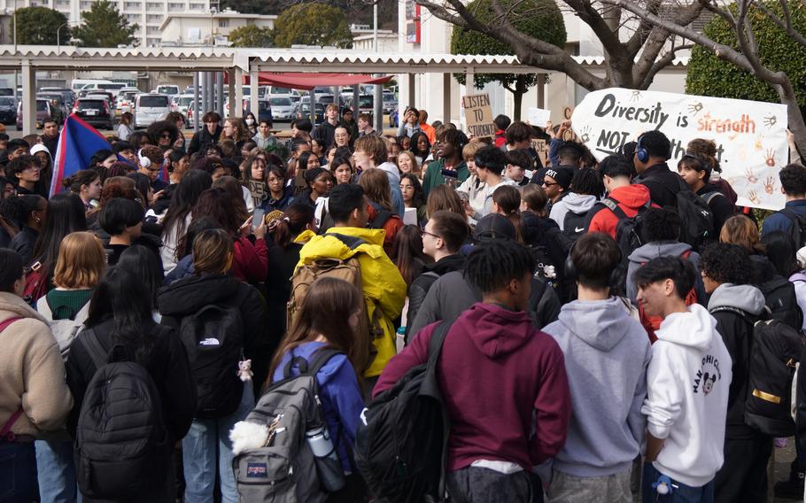 A crowd of students, some holding signs, stand in a school courtyard.