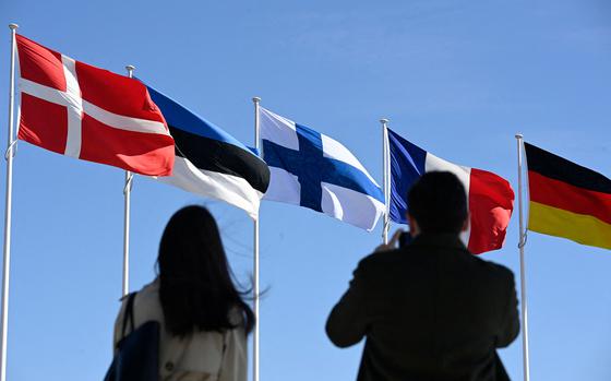 People stand in front of the Finnish national flag (center) after a flag-raising ceremony at the NATO headquarters in Brussels, on Tuesday, April 4, 2023. Finland became the 31st member of NATO, wrapping up its historic strategic shift with the deposit of its accession documents to the alliance. (John Thys/AFP/Getty Images/TNS)