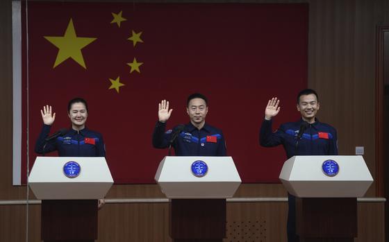 Three astronauts wave as they stand behind podiums on a stage.