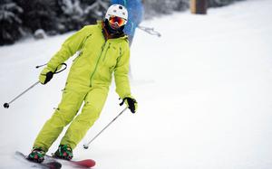 A man in a green snow suit and white helmet skis down a snowy slope.