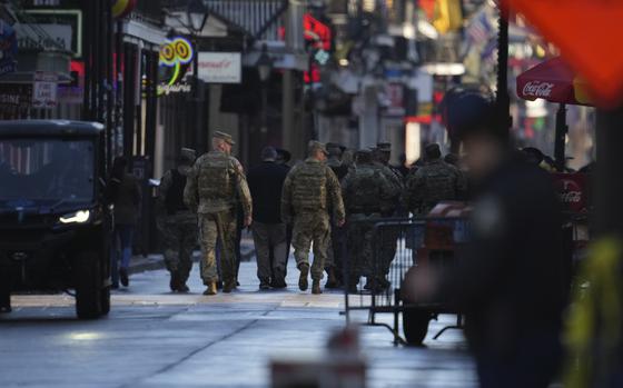 A view of Bourbon Street in New Orleans from ground level, with military service members walking down the street in camouflage uniforms.