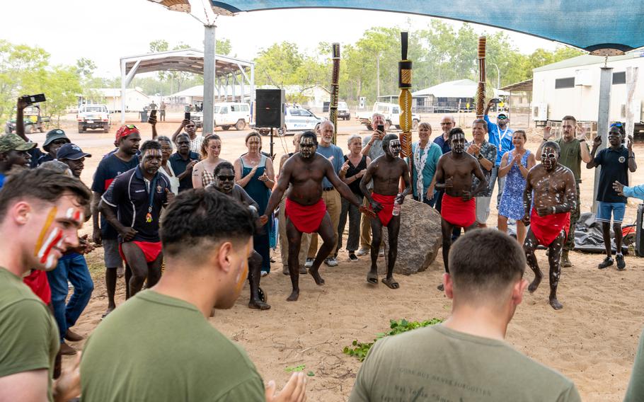 Pukumani people wearing red loincloths stand in front of Marines during a ceremony.