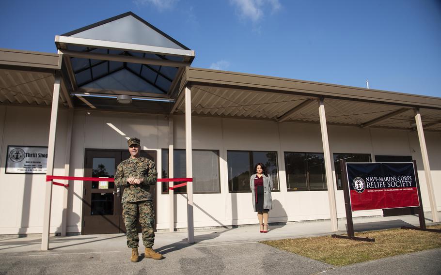 A Marine in camouflage uniform stands in front of a store entrance with a red ribbon across it.