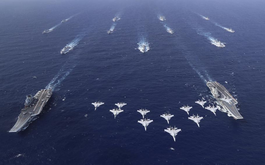 An array of Chinese military ships, seen from above, sails in formation in open ocean.