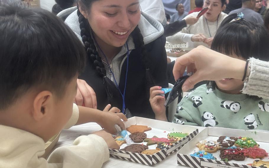 A soldier smiles as she helps children decorate cookies.