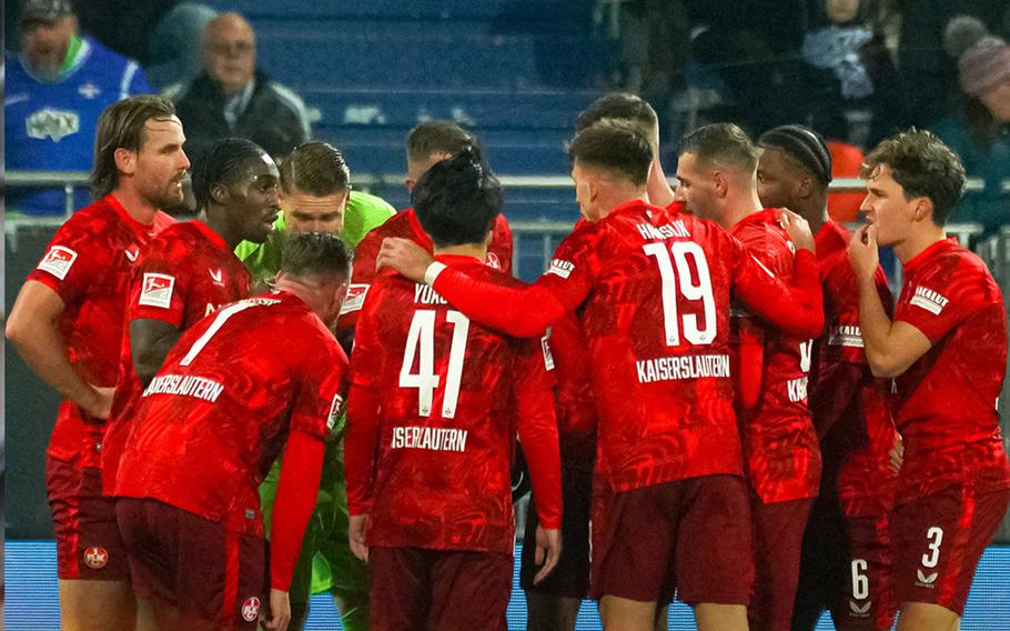 1. FC Kaiserslautern players wearing red uniforms come together for a huddle.