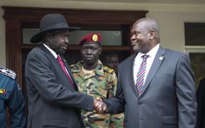 Two men in suits shake hands, with a man in a military uniform between them.