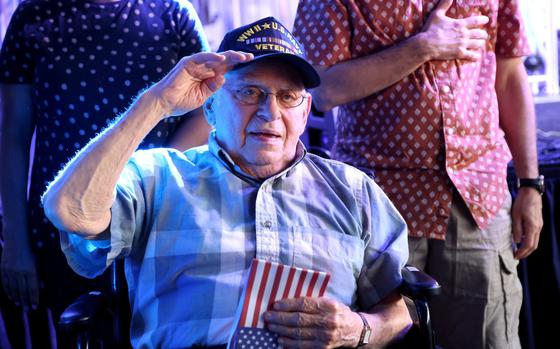 World War II veteran Arthur Grabiner salutes while holding an American flag.