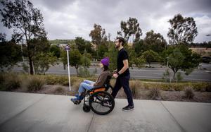 Connor Mayer pushes his wife, Courtney Gavin, in a wheelchair as they go outside for fresh air on Tuesday, Feb. 14, 2023, in Irvine, California. Courtney got sick with COVID-19 in March 2020 and is now sick with long covid. She gets help from her husband doing basic tasks at home. (Allen J. Schaben/Los Angeles Times/TNS)