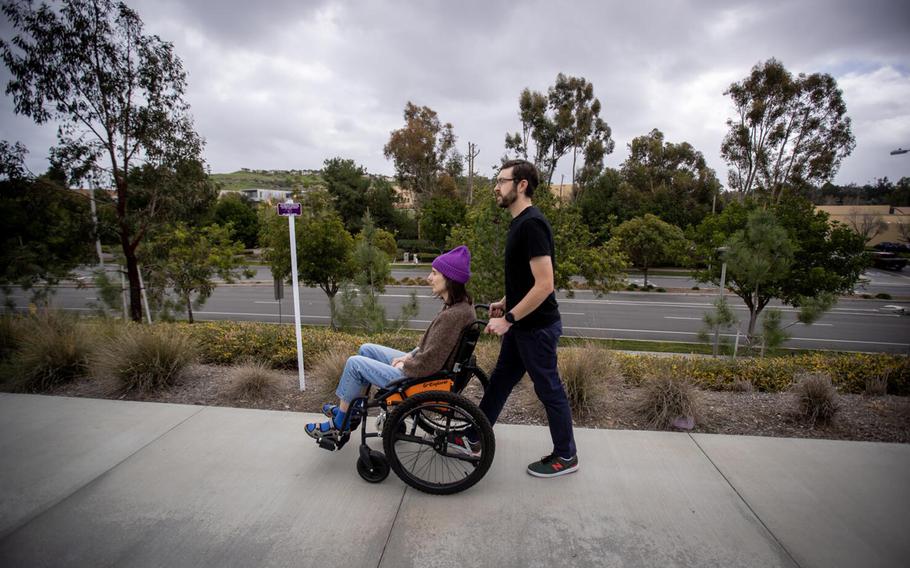 Connor Mayer pushes his wife, Courtney Gavin, in a wheelchair as they go outside for fresh air on Tuesday, Feb. 14, 2023, in Irvine, California. Courtney got sick with COVID-19 in March 2020 and is now sick with long covid. She gets help from her husband doing basic tasks at home. 