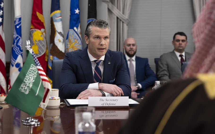 Hegseth sitting at a table with flags and others seated behind as he speaks.