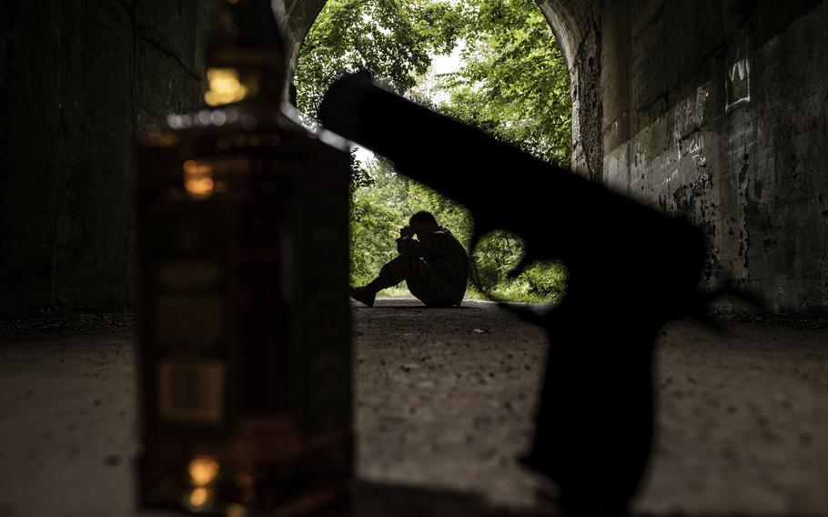 A gun and a liquor bottle in the foreground with a person seated in a shadow