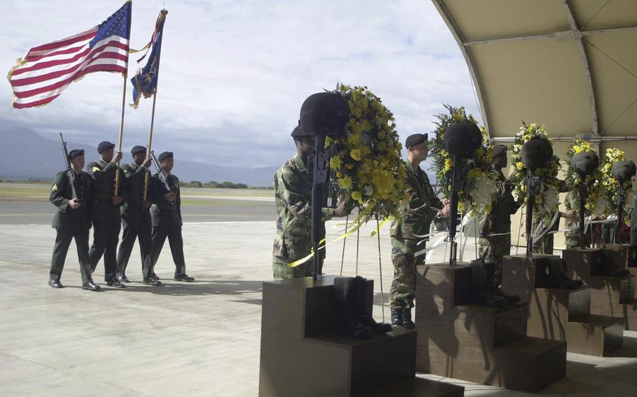 A memorial service with four soldiers carrying a U.S. flag in front of several wreaths.