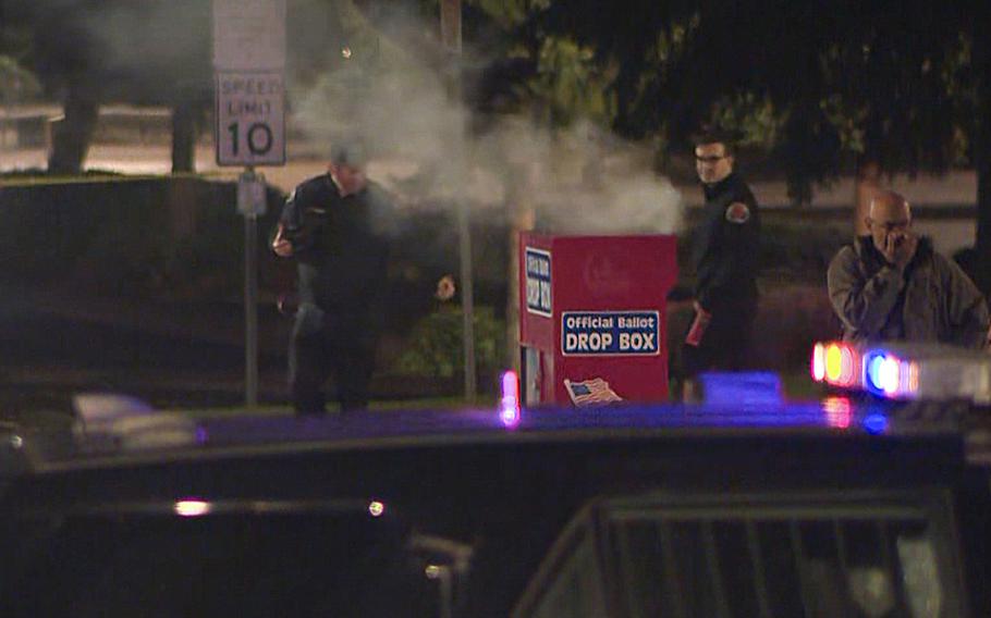 Emergency officials surround a smoldering ballot box.