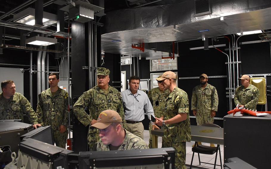 A group of Navy leaders watch sailors at work.