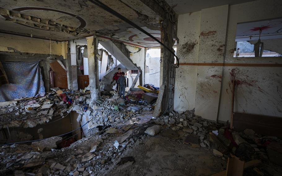 Two children look through a concrete building that has a large hole in the floor and scattered debris.