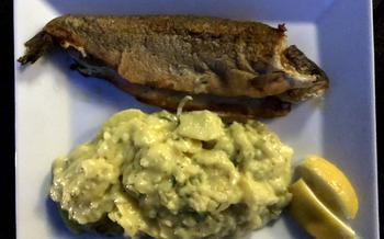 A whole cooked trout on a plate with potato salad