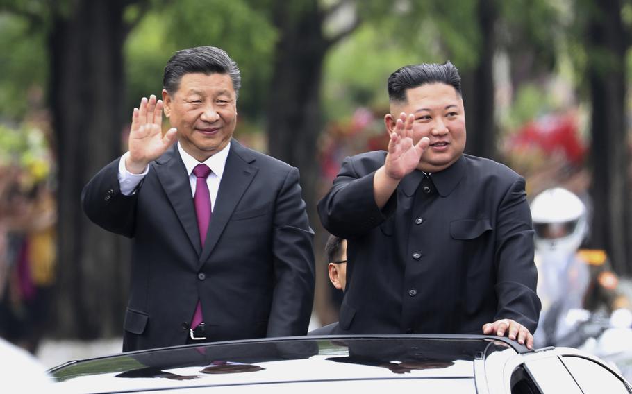 Chinese President Xi Jinping and North Korean leader Kim Jong Un stand through the sun roof of an open top limousine and wave to the crowd in North Korea.