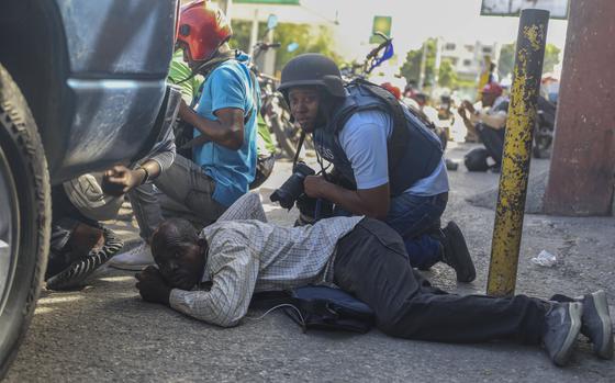 Journalists in flak jackets and helmets kneel behind a car.