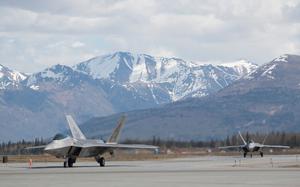 Two fighter jets on a runway with snow-capped mountains in the background.