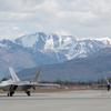 Two fighter jets on a runway with snow-capped mountains in the background.