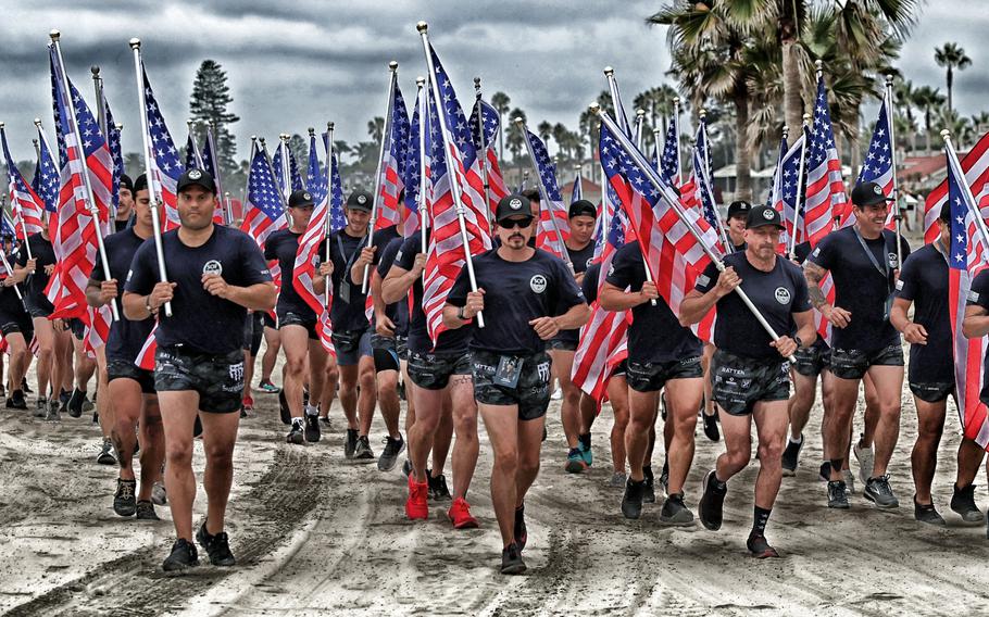 Swimmers run in a formation on the beach while carrying American flags