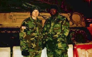 Michael Trotter stands in front of a military tracked vehicle with a fellow soldier in uniform.