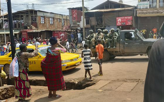 M23 troops in a truck drive down a street as citizens look on.